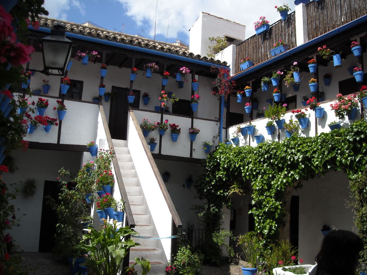 Un patio cordobés con macetas azules y flores en la galería