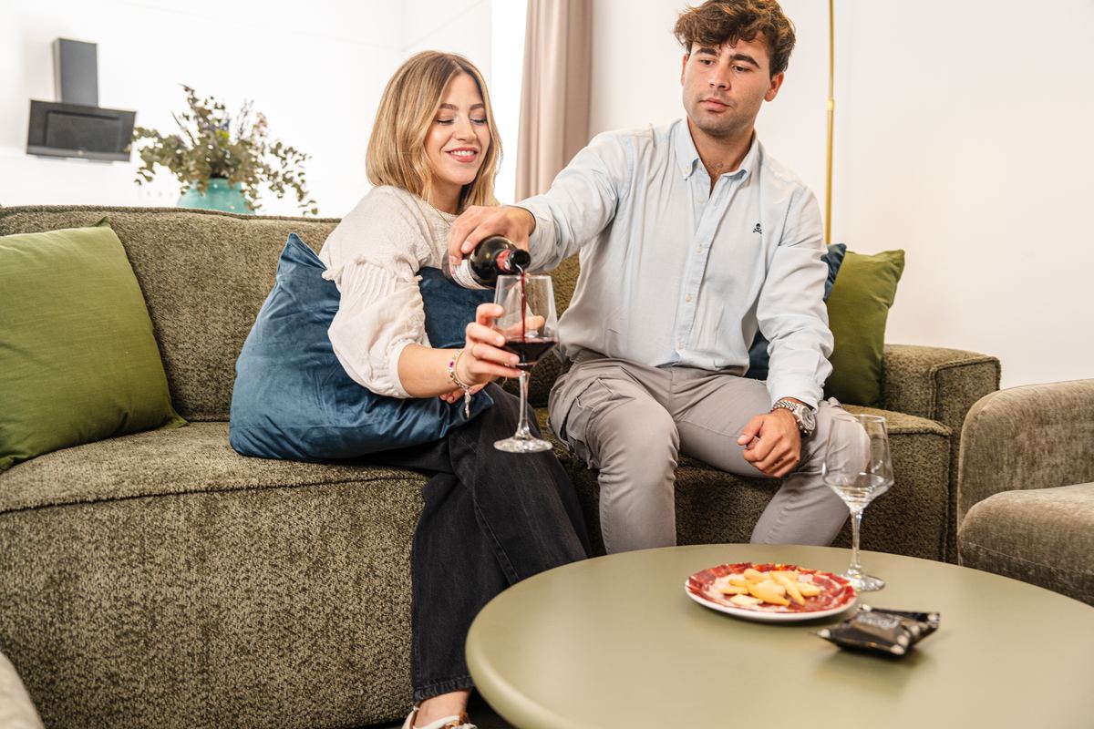Dos huéspedes brindan con vino tinto en el sofá del apartamento